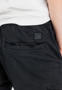 Zwarte cargoshorts gemaakt van lichtgewicht stof, met een achterzak voorzien van een vierkante label met de tekst "ALPHA INDUSTRIES" en een subtiele textuur.