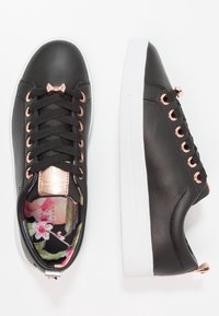 Černé syntetické tenisky s růžovými zlatými očky, texturovaným černým svrškem, bílou podrážkou a podšívkou s květinovým vzorem.