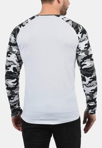 Langsleeve shirt met een witte body en een zwart/grijs camouflagepatroon op de mouwen. Gemaakt van stof met een gladde textuur, reguliere pasvorm.