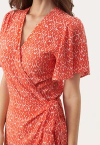 Rotes und weißes gemustertes Wickelkleid mit kurzen Puffärmeln, aus weichem Stoff, mit V-Ausschnitt und Knotendetail an der Taille.