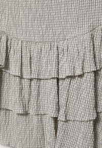 Beżowa tkanina z czarnym wzorem w kratę, ozdobiona warstwowymi falbanami i o teksturze lekko pomarszczonej.