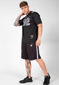 Zwart sportshirt met zilveren nummer "32" en logo, gecombineerd met zwarte shorts met zijstrepen en grafische accenten, beide in een gestructureerde stof.