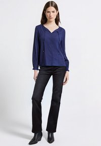 Blusa blu navy con maniche lunghe, scollo con coulisse, texture liscia e vestibilità rilassata, abbinata a jeans neri a gamba dritta e stivaletti alla caviglia.