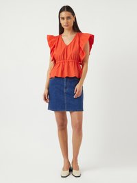 Rød bomulds bluse med flæser på ærmerne og V-udskæring, parret med en blå denim miniskirt. Modellen har crèmefarvede blokhælede sko på.
