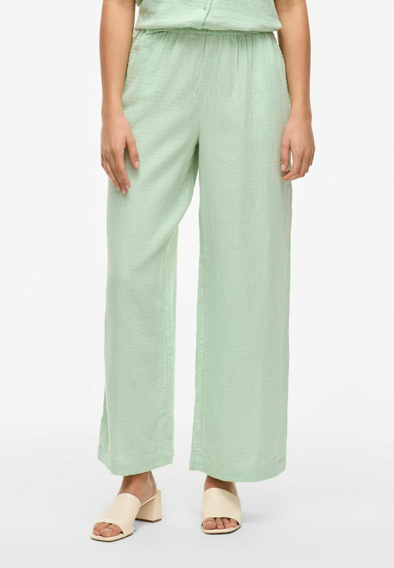 Lichtgroene rechte broek van een gestructureerde stof, met een elastische tailleband en een relaxte pasvorm. Draagt bij beige open-teen hakken.