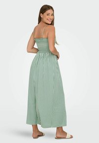 Strapless grön och vit randig maxiklänning med smockad bysta, flödande kjol och platta sandaler. Slätt tyg, lätt textur.