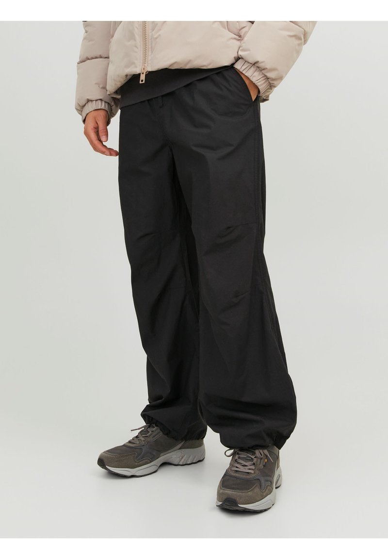 Pantalones negros, holgados y de textura suave. Cuentan con una cinturilla elástica. Combinados con zapatillas deportivas grises y una chaqueta de plumas ligera.