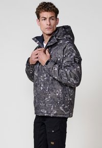 Chaqueta acolchada en gris oscuro con un patrón texturizado. Presenta una capucha, cierre frontal y un acento negro en la manga. Diseño de corte slim.
