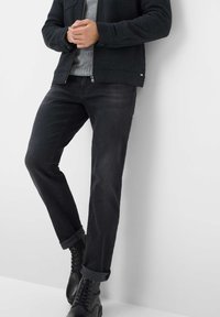 Jeans di denim nero con orli arrotolati, abbinati a un maglione di lana grigia e stivali neri con lacci, su uno sfondo bianco semplice.