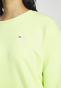 Felpa verde fluorescente realizzata in tessuto morbido. Presenta un collo a girocostina e il logo "Fila" ricamato in rosso e bianco.