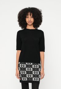 Μαύρο τοπ με κοντά μανίκια και απαλή υφή, συνδυασμένο με φούστα σε μαύρο και λευκό χρώμα με περίτεχνα σχέδια.