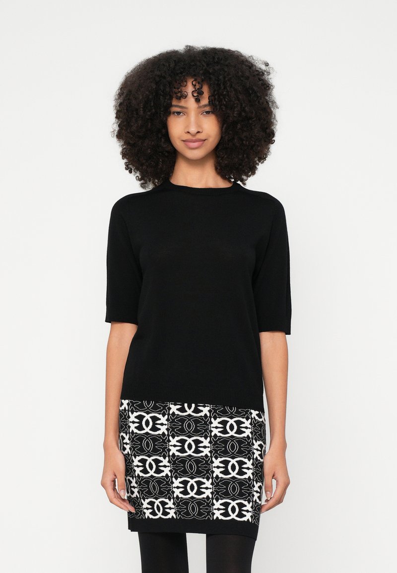 Μαύρο τοπ με κοντά μανίκια και απαλή υφή, συνδυασμένο με φούστα σε μαύρο και λευκό χρώμα με περίτεχνα σχέδια.