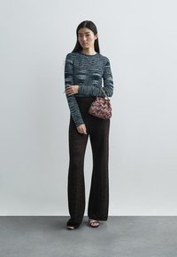 Striped long-sleeve top in blue and gray, paired with textured black flared pants. Features a red and patterned handbag, and strappy black heels.