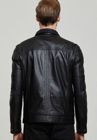 Zwarte leren jas met een aansluitend ontwerp, zichtbare stiksels en schouderaccenten. Heeft een strakke, gladde textuur.