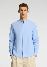 Svijetloplave košulje dugih rukava s ovratnikom, s blagom teksturom; uparen s bež hlačama ravnog kroja.