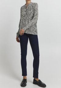 Blusa a maniche lunghe con motivo zebra in bianco e nero, con scollatura a bottoni, abbinata a jeans skinny scuri e mocassini neri.