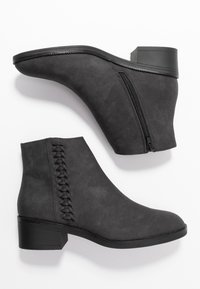 Botas negras hasta el tobillo hechas de suave gamuza con un zipper lateral y un detalle trenzado a lo largo del costado exterior. Tacón cuadrado y textura suave.