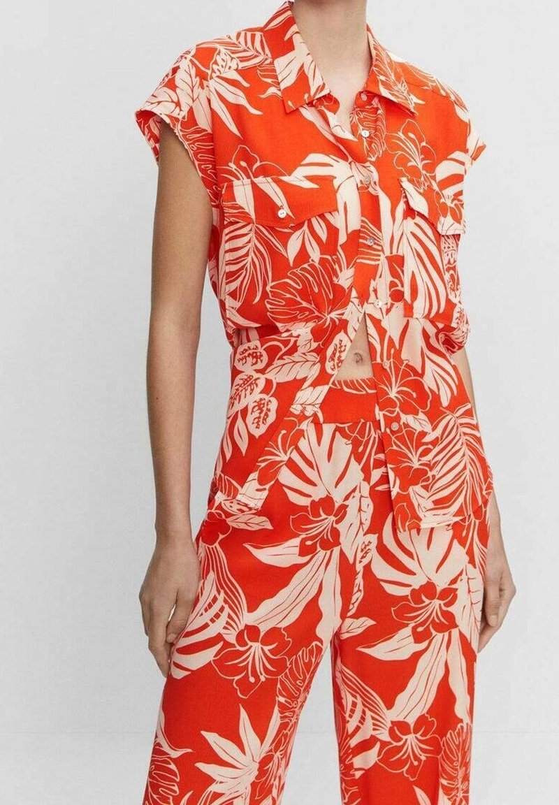 Top corto floreale rosso con maniche corte e chiusura a bottoni, abbinato a pantaloni a vita alta con un motivo di foglie tropicali.