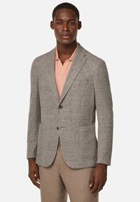 Grå texturerad blazer med två framfickor och en-knapps stängning. Bärs över en ljusrosa polo skjorta, matchad med beige byxor.