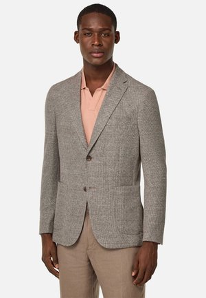 Grauer strukturierter Blazer mit zwei Fronttaschen und einem Ein-Knopf-Verschluss. Getragen über einem hellrosa Polohemd, kombiniert mit beigen Hosen.