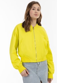 Giacca bomber gialla con zip frontale, polsini e orlo a costine. Tessuto liscio, design corto e tasche laterali.