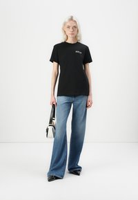 Black cotton t-shirt with "REPLAY" logo in white, paired with light blue wide-leg jeans. Model holds a two-tone handbag, black and white.