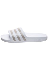 Sandale slide blanche en matériau synthétique, avec trois bandes horizontales beiges sur le dessus, une semelle texturée et un logo embossé sur le côté.