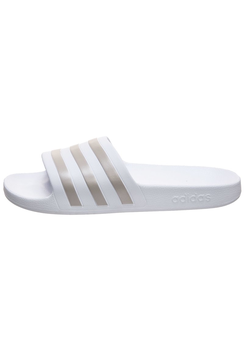 Sandale slide blanche en matériau synthétique, avec trois bandes horizontales beiges sur le dessus, une semelle texturée et un logo embossé sur le côté.