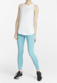 Top sin mangas blanco combinado con leggings azul claro con destellos, diseñado para ropa deportiva, rematado con zapatillas deportivas negras.