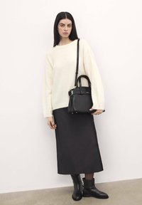 Black leather handbag with short and long straps, paired with a cream oversized sweater and a long black satin skirt. Black ankle boots complete the look.