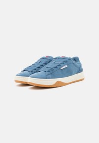 Blå semskede sneakers med rund tå, flate snøringer og hvit mellomsåle. Har gummisåle og en liten logoakkent på siden.