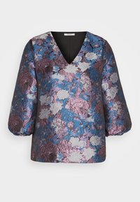 Blouse florale en violet, bleu et argent avec un tissu texturé. Présente un décolleté en V et des manches bouffantes pour une silhouette structurée.