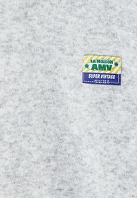 Tessuto grigio di felpa con una consistenza morbida, caratterizzato da un'etichetta colorata che recita "LA MAISON AMV SUPER VINTAGE" in verde, giallo e blu.