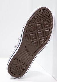 Gumová podrážka bílé plátěné tenisky nakloněná proti bílé backgroundu s vzorovaným vzorkem a značkou "Converse All Star".