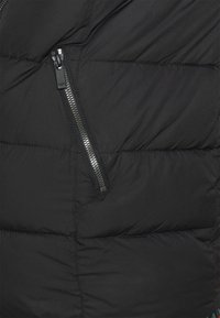 Sección de chaqueta acolchada negra con un bolsillo diagonal con cremallera. Material acolchado con una textura suave y un sutil detalle de costura.