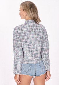 Teksturirana, višebojna tweed jakna s skraćenim dizajnom, koja ima visoki ovratnik i duge rukave, u paru s izlizanim trapericama.