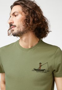 Oliven grøn t-shirt i bomuld med rund hals, der har et broderet fiske-design og teksten "FISHING THERAPY" på brystet.