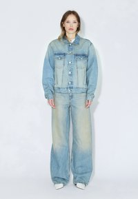 Veste en jean bleu clair et jean à jambes larges avec une finition délavée. Comprend deux poches poitrine, des éléments en métal argenté et une coupe décontractée.