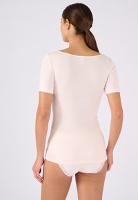 Camiseta ajustada de color rosa claro con mangas cortas, textura suave y un escote amplio; combinada con ropa interior blanca de canalé con detalles de encaje.