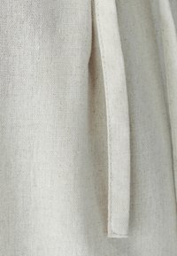 Krupni načrt bež grobe tkanine z vgrajenim pravokotnim trakom ali vrvico, ki visi vertikalno.