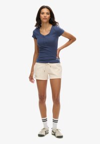 Haut à manches courtes côtelé bleu marine avec patte de boutonnage, associé à un short beige à cordon de serrage. Comprend des chaussettes rayées noires et blanches et des baskets décontractées.