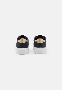 Navy fabric sneakers with gold accents and white rubber soles. Features a padded collar and embossed logo detail on the heel.