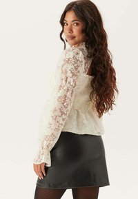 Witte bloemenkant blouse met pofmouwen, gelaagd over een gerimpeld detail, gecombineerd met een zwarte leren minirok.