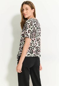 Camiseta de manga corta en tejido ligero, con un patrón abstracto en negro, rosa y blanco. Corte ligeramente holgado y escote redondo.