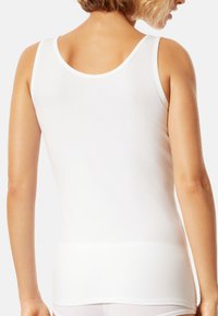 White tank top with a rounded neckline and thin straps. Made of smooth fabric, it features a close fit and seamless design. No visible logos.