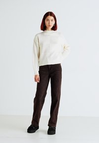 Sweater de malha creme com patches de textura vertical, combinado com calças de algodão largas em corduroy castanho e sapatos de plataforma pretos com sola decorativa.