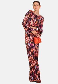 Conjunto de dos piezas impreso que incluye una blusa de manga larga corta y pantalones de pierna ancha en un vibrante diseño floral multicolor. Los accesorios incluyen un bolso naranja.