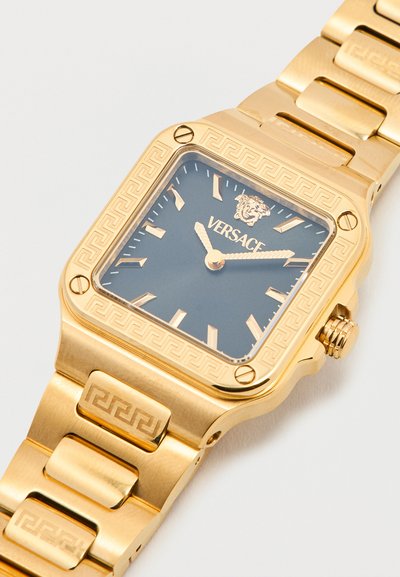Χρυσό ρολόι Versace με τετράγωνο μαύρο καντράν, λογότυπο Medusa, γεωμετρικό σχέδιο στην στεφάνη και το βραχιόλι, δείχνοντας ώρα 10:10.