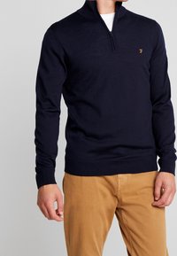 Navyblå zip-up tröja med strukturerad stickning, med en liten logotyp på bröstet och ribbade ärmslut och nederkant. Matchad med beige byxor.