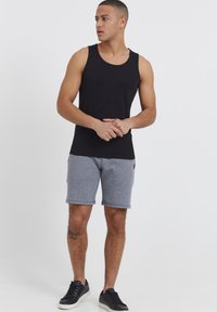 Zwarte tanktop gecombineerd met grijze shorts met een gestructureerd patroon. De shorts hebben een klein logootje en zijn gestyled met zwarte sneakers.